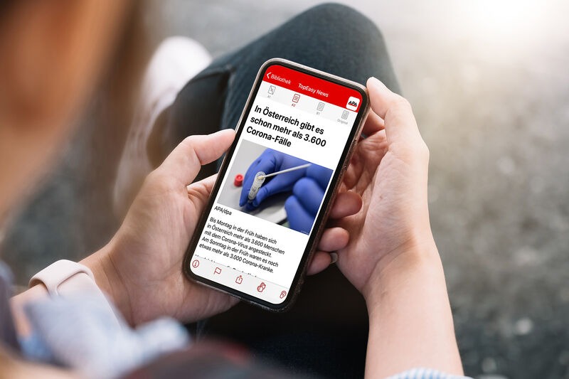 Frau sitzt mit ihrem Handy in den Händen und blickt auf Bildschirm, zeigt Nachrichten in leicht verständlicher Sprache in der capito App